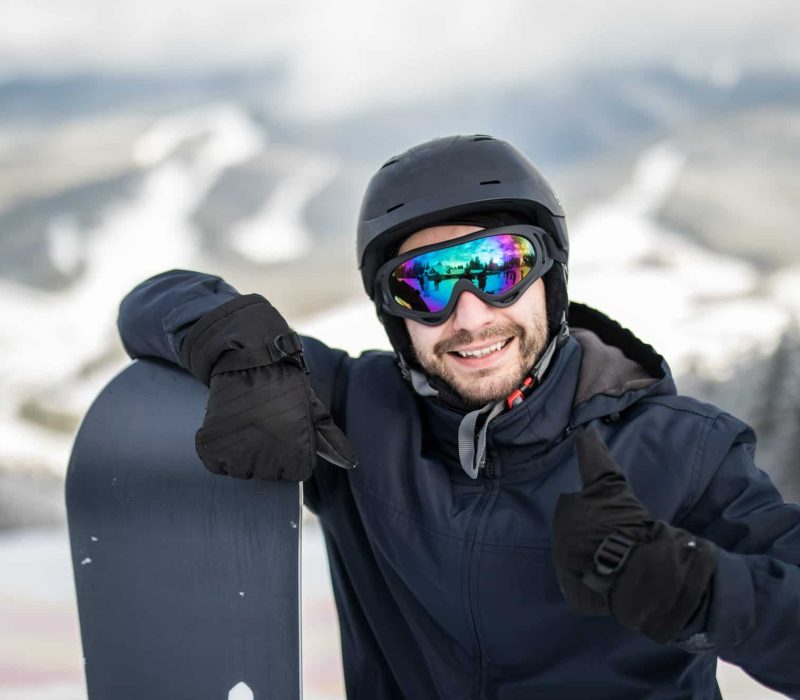 man-snowboarder-standing-top-snowy-slope-with-snowboard-smiling-camera-showing-thumbs-up-winter-ski-resort